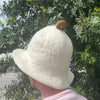 A soft off-white felt sauna bowl hat with a fluffy brown pom-pom on top for cozy sauna use
