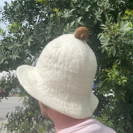 A soft off-white felt sauna bowl hat with a fluffy brown pom-pom on top for cozy sauna use
