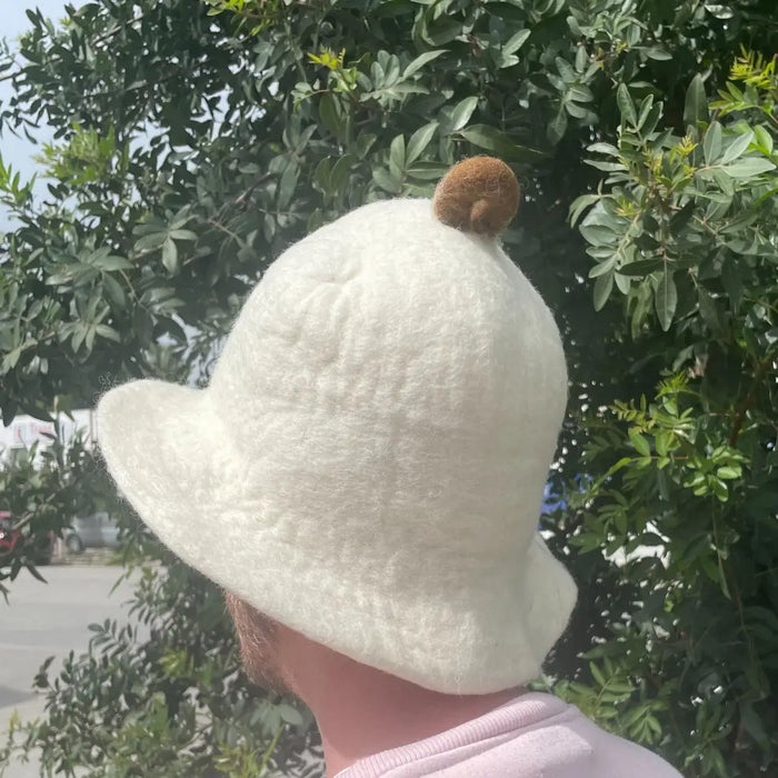 A soft off-white felt sauna bowl hat with a fluffy brown pom-pom on top for cozy sauna use