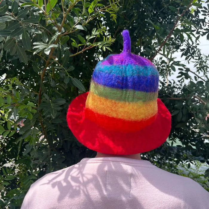 A felted sauna bowl hat in rainbow stripes with a purple tufted top made from soft felt material