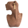 A gold-toned festive fir leaf earring with a textured glittery finish hanging on a woven brown stand