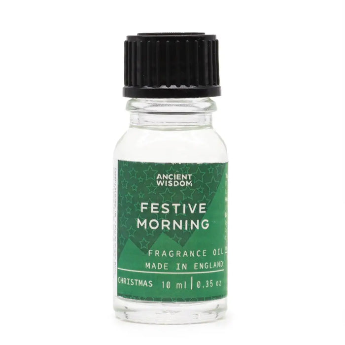 A clear glass bottle with black ribbed cap and green label reading ancient wisdom festive morning fragrance oil for christmas use