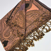 A soft peach and brown pashmina scarf with paisley patterns and black detailing with fringed edges
