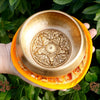 Golden five buddha singing bowl with intricate engravings resting on an orange silk cushion 10cm size