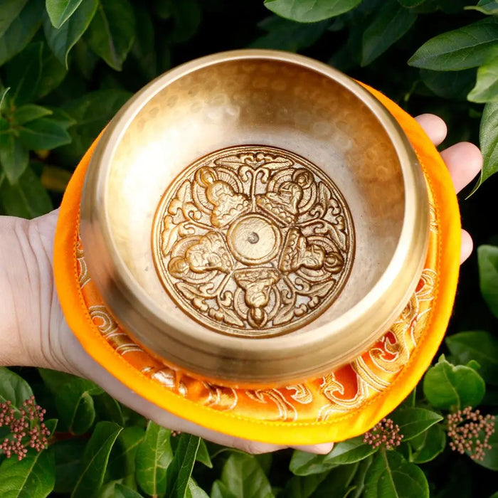 Golden five buddha singing bowl with intricate engravings resting on an orange silk cushion 10cm size