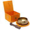 Golden five buddha singing bowl with hammered surface and engraved patterns on orange mat next to wooden mallet