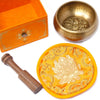 Golden five buddha singing bowl with intricate engravings resting on a yellow embroidered cushion