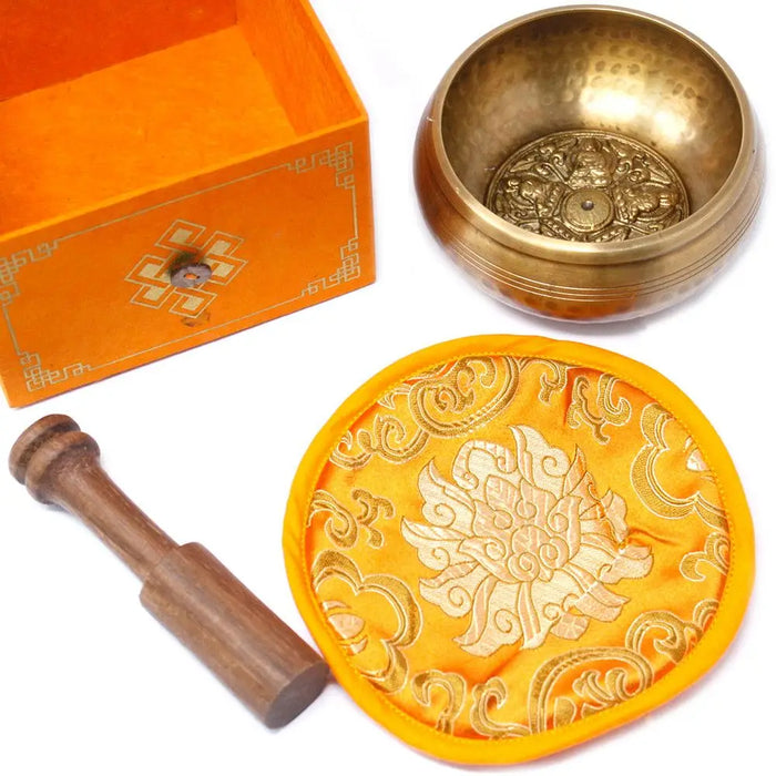 Golden five buddha singing bowl with intricate engravings resting on a yellow embroidered cushion