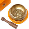 Golden five buddha singing bowl with intricate engravings resting on an orange cushion in a 10cm set