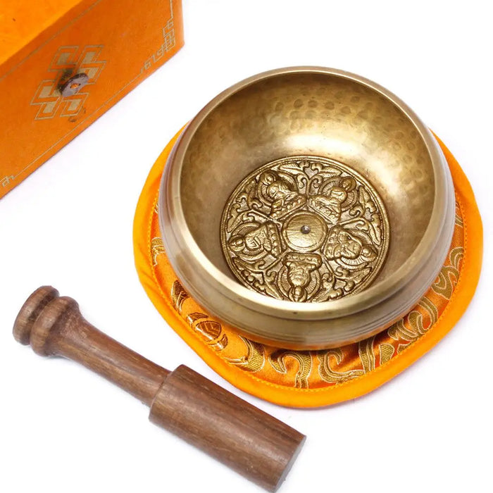 Golden five buddha singing bowl with intricate engravings resting on an orange cushion in a 10cm set