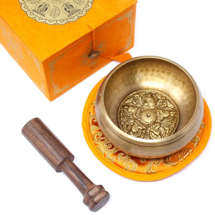 Golden five buddha singing bowl with intricate engravings resting on an orange cushion in a 10cm set