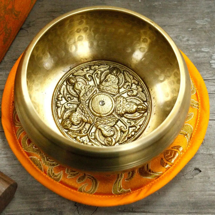 Golden five buddha singing bowl with intricate engravings resting on an orange cushion in a 10cm set