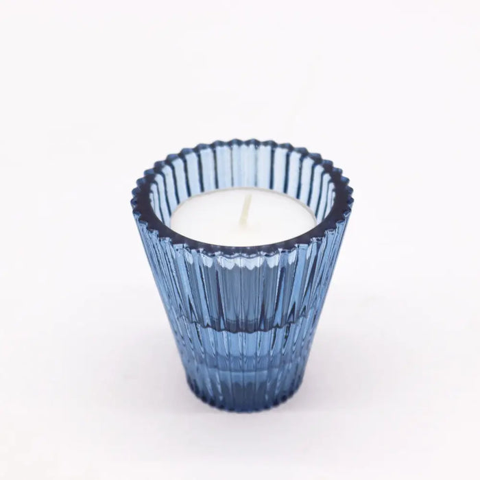 A royal blue glass flip dinner candle holder with vertical ridges and scalloped rim holding a white candle