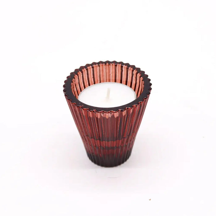 A deep red glass flip dinner candle holder with vertical ridges holds a white tealight candle for candles use