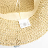 Beige woven floppy straw sun hat with matching fabric band and small embroidered logo tag with blue flowers design