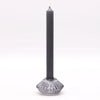 A sleek matte black dinner candle stands in a clear faceted glass tealight holder with a geometric base for candles