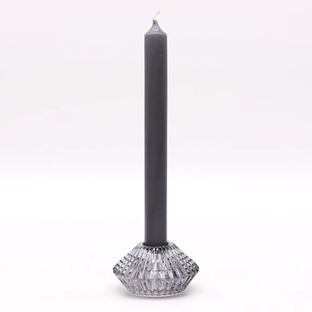A sleek matte black dinner candle stands in a clear faceted glass tealight holder with a geometric base for candles
