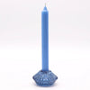 A solid blue flower flip dinner candle stands in a matching translucent glass tealight holder with a diamond base