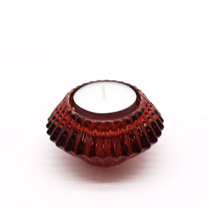A deep red faceted glass flower flip dinner tealight holder with scalloped edge holding a white candle