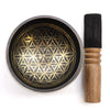 A black life singing bowl set with a golden flower of life pattern and a wooden mallet on a ring pillow