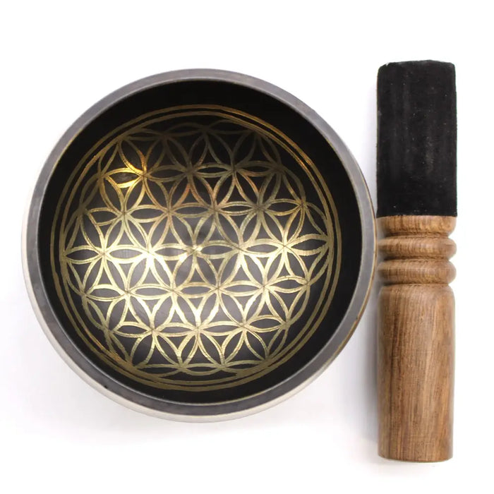 A black life singing bowl set with a golden flower of life pattern and a wooden mallet on a ring pillow