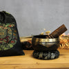 Black tibetan life singing bowl with gold rim and engraved patterns resting on a matching embroidered ring pillow