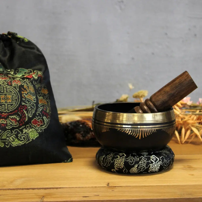 Black tibetan life singing bowl with gold rim and engraved patterns resting on a matching embroidered ring pillow