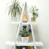 White painted folding albesia wood a frame ladder shelf with three tiers holding plants and a salt lamp