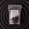 A clear pouch of dark grey luxury black candle sand by ancient wisdom for fragranced bright bergamot candles 300g