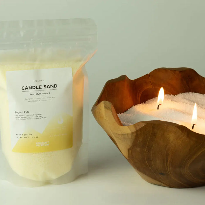 A rustic wooden bowl filled with white candle sand and two lit regent polo fragranced cream candles