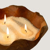 A rustic wooden bowl with three lit candles resting in white coarse-grained regent polo candle sand