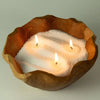 A rustic wooden bowl filled with white candle sand and three lit candles labeled starlight elixir 300g