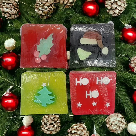 Four colorful handmade soap slices in red green and black with christmas themes like holly santa hat and tree designs