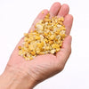 A hand holds small irregular yellow and cream-colored golden quartz chips made of crushed quartz fragments