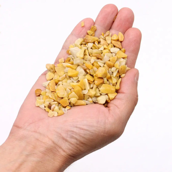 A hand holds small irregular yellow and cream-colored golden quartz chips made of crushed quartz fragments
