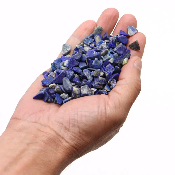 A hand holds rough blue lapis lazuli gemstone chips with natural white and gray veining weighing one kilogram