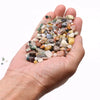 A hand holds mixed natural gemstone chips in various smooth polished colors and sizes totaling 1kg