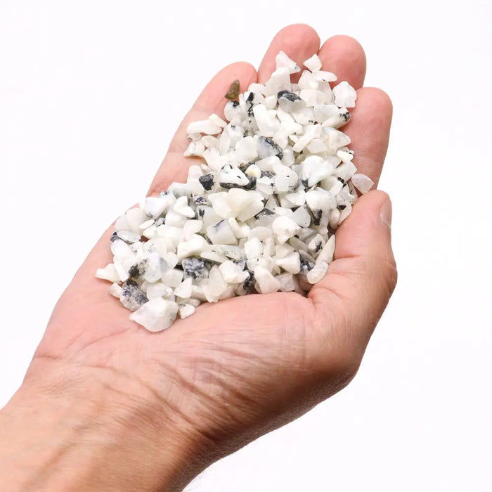A hand holding white and black speckled rainbow moon gemstone chips in irregular shapes totaling 1kg weight