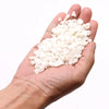 A hand holds a pile of small smooth white quartz gemstone chips weighing approximately one kilogram