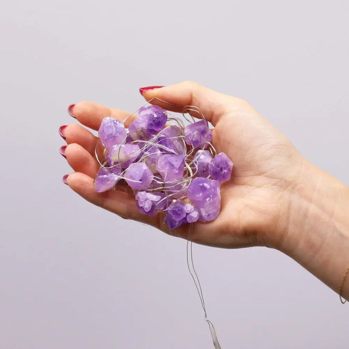 A hand holds purple amethyst crystal enchantment lights with silver wire string for decorative use