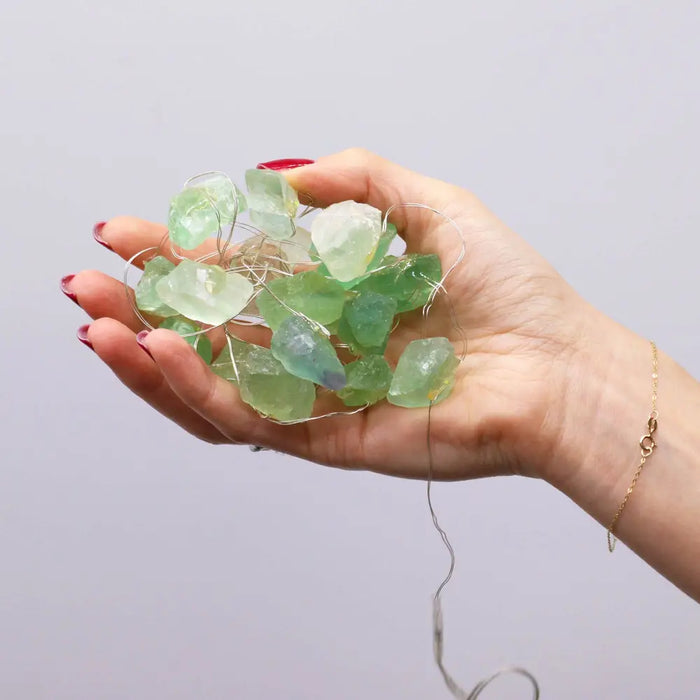 A delicate string of translucent green crystal jade beads with natural facets and thin wire wrapping for enchantment lights