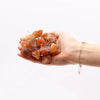 A hand holds translucent amber orange jade stones with thin silver wire as enchantment lights gemstones
