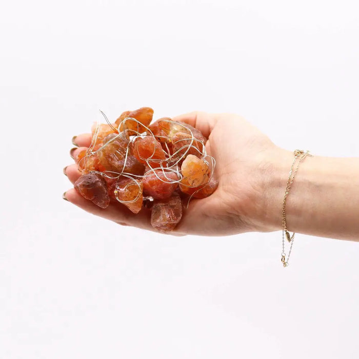 A hand holds translucent amber orange jade stones with thin silver wire as enchantment lights gemstones