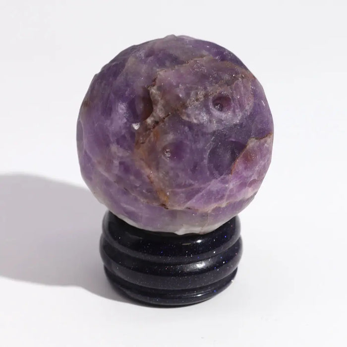 A polished purple amethyst gemstone planet sphere with natural crystals and brown inclusions on a black solar stand