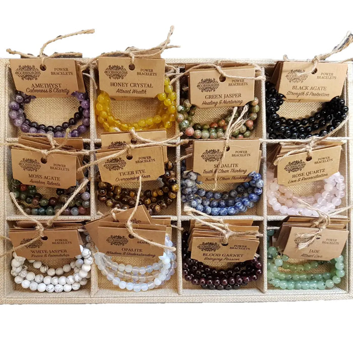 A collection of colorful gemstone power bracelets in purple yellow green black blue white and pink with mood stone labels