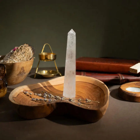 A clear quartz six face obelisk point with natural inclusions on a wooden tray for meditation spaces
