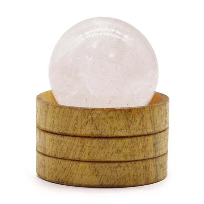 A translucent white clear quartz gemstone sphere sits on a stacked wooden base with visible grain pattern