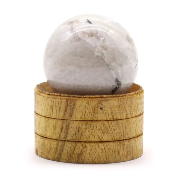 A translucent white indian moonstone sphere with gray veining resting on a stacked wooden base 40mm gemstone sphere