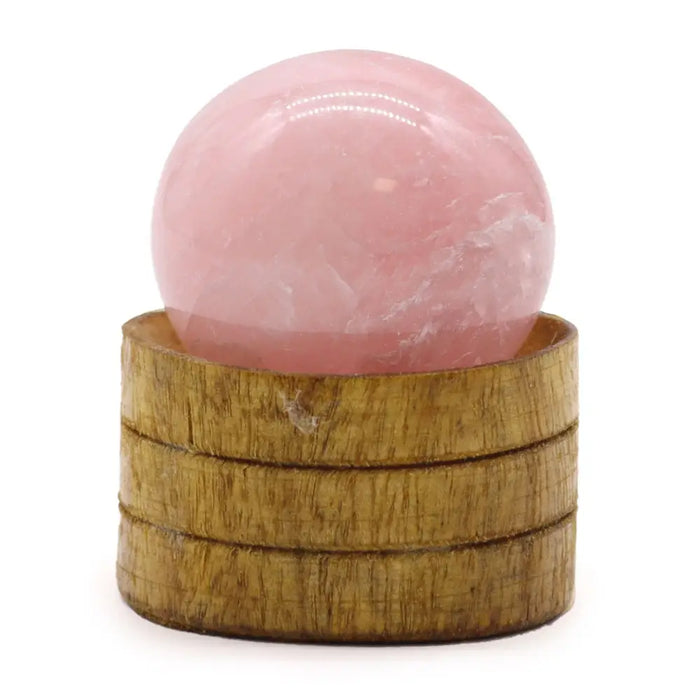 A smooth translucent pink rose quartz gemstone sphere 40mm resting on a stacked wooden base