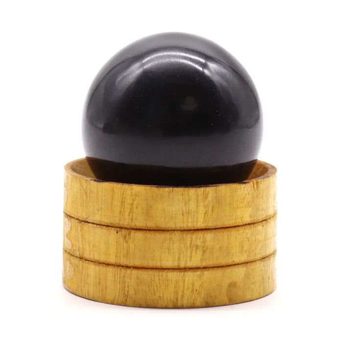 A smooth glossy black tourmaline gemstone sphere 40mm resting on a stack of four light golden wooden rings